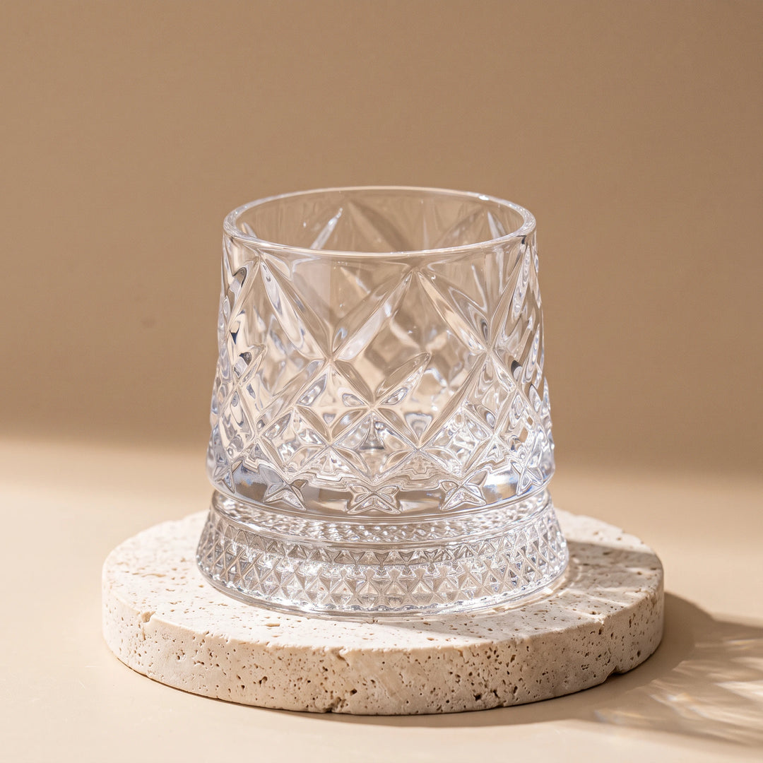 Diamond-pattern crystal spinning whiskey glass on a travertine coaster